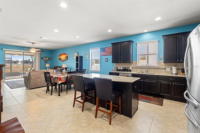 kitchen with a sink, a kitchen island, a kitchen breakfast bar, open floor plan, and freestanding refrigerator