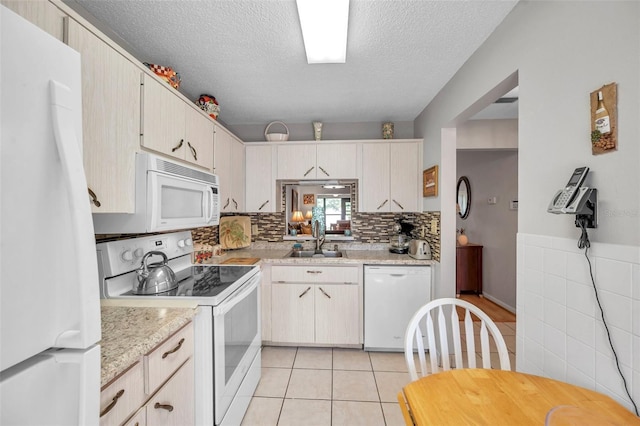 kitchen with light tile patterned flooring, sink, backsplash, white appliances, and a textured ceiling