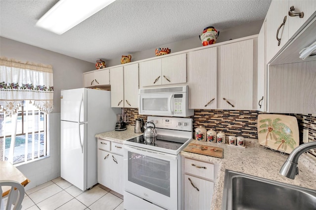 kitchen featuring sink, decorative backsplash, light tile patterned floors, white appliances, and a textured ceiling