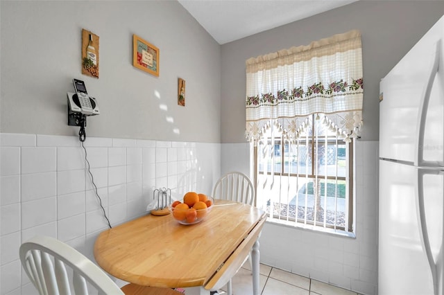 dining space featuring light tile patterned flooring and tile walls