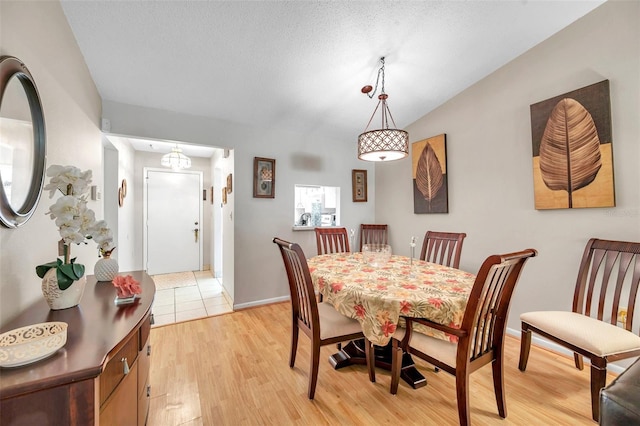 dining room with lofted ceiling, light hardwood / wood-style flooring, and a textured ceiling