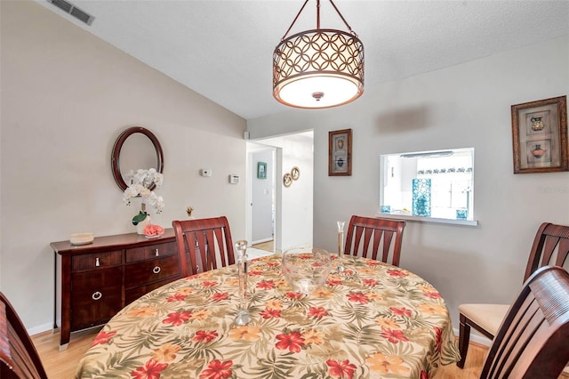 dining room featuring lofted ceiling, light hardwood / wood-style floors, and a textured ceiling