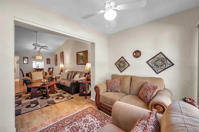 living room with ceiling fan, vaulted ceiling, a textured ceiling, and light wood-type flooring