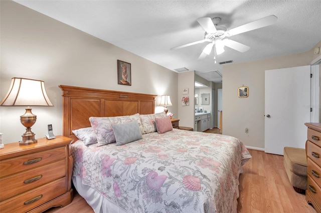 bedroom with lofted ceiling, light hardwood / wood-style flooring, ceiling fan, ensuite bathroom, and a textured ceiling