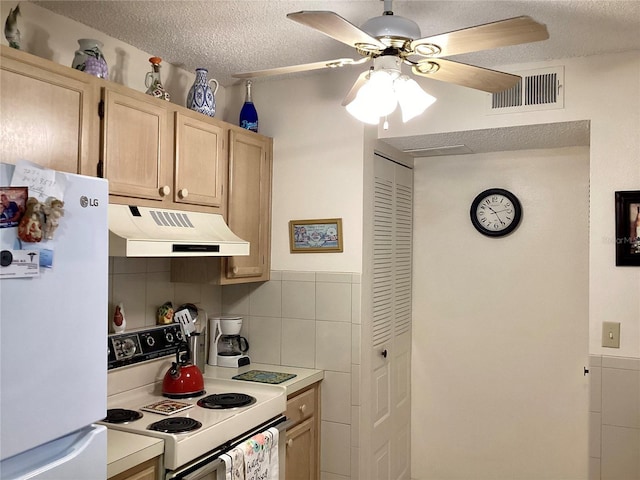 kitchen with white appliances, under cabinet range hood, a textured ceiling, visible vents, and light brown cabinets