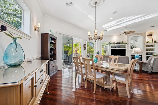 dining space featuring a fireplace, ceiling fan with notable chandelier, dark wood-type flooring, and ornamental molding