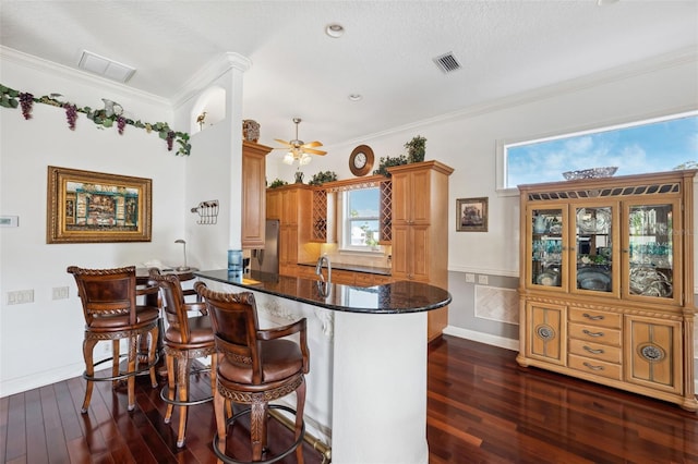 kitchen with ornamental molding, kitchen peninsula, dark stone counters, and a kitchen bar