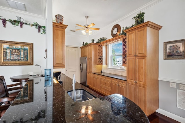 kitchen with sink, crown molding, ceiling fan, dark stone countertops, and stainless steel fridge with ice dispenser