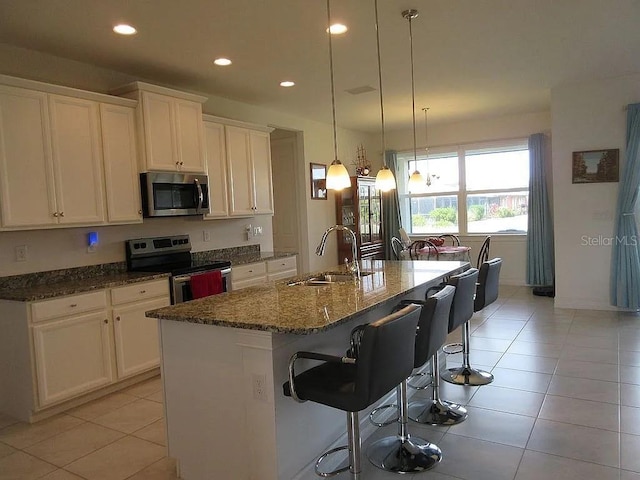 kitchen featuring a kitchen bar, sink, hanging light fixtures, stainless steel appliances, and a kitchen island with sink