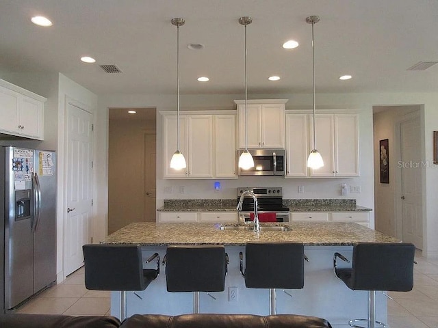 kitchen with stainless steel appliances, hanging light fixtures, a center island with sink, and white cabinets