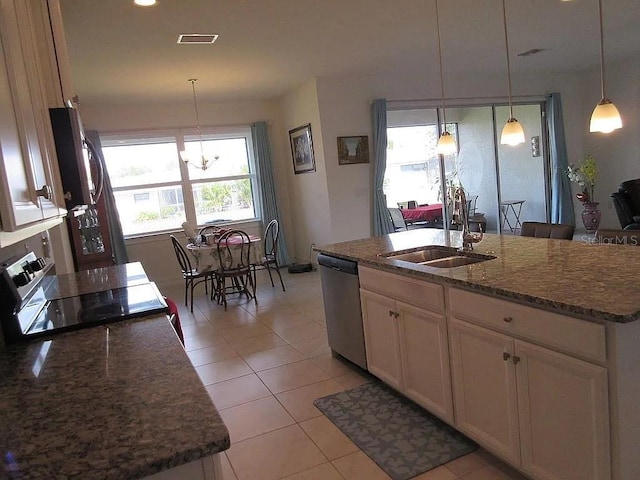 kitchen featuring pendant lighting, stainless steel appliances, dark stone counters, and a center island with sink