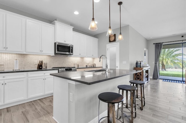 kitchen with decorative light fixtures, sink, backsplash, stove, and a kitchen island with sink