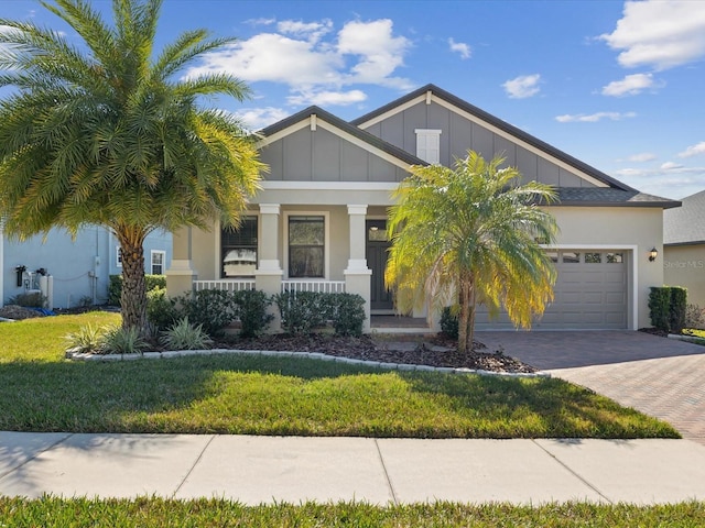 craftsman house with decorative driveway, covered porch, board and batten siding, a front yard, and a garage