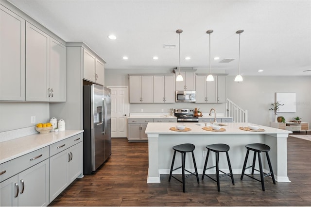 kitchen featuring sink, gray cabinets, stainless steel appliances, an island with sink, and decorative light fixtures