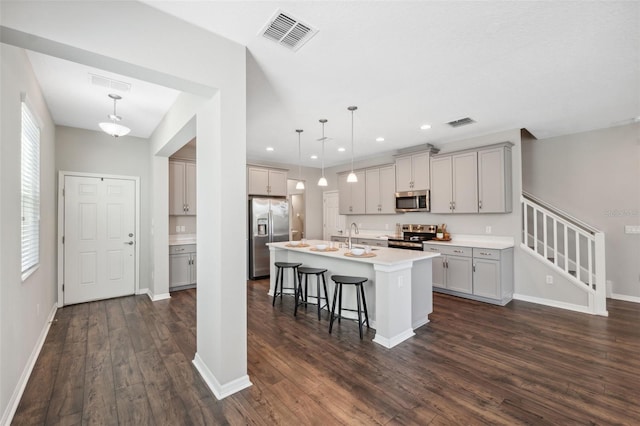 kitchen with appliances with stainless steel finishes, a kitchen island with sink, hanging light fixtures, gray cabinetry, and a kitchen bar