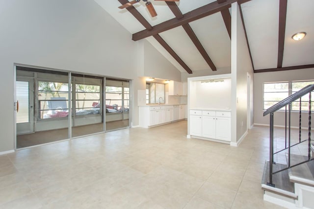 unfurnished living room with ceiling fan, high vaulted ceiling, beam ceiling, and sink