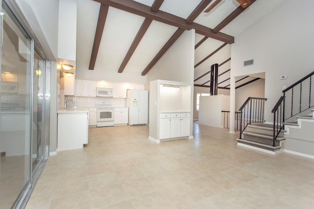 kitchen with sink, white appliances, beam ceiling, high vaulted ceiling, and white cabinets