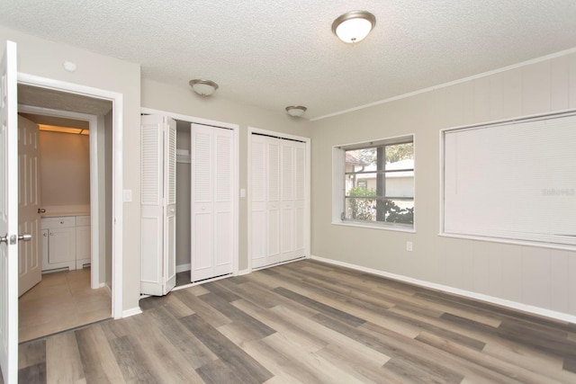 unfurnished bedroom with hardwood / wood-style floors, two closets, and a textured ceiling