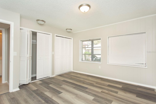 unfurnished bedroom with dark wood-type flooring, a textured ceiling, and two closets