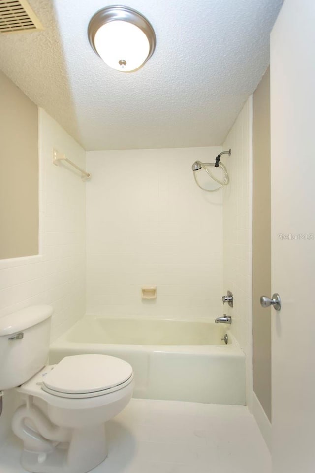 bathroom featuring tiled shower / bath, a textured ceiling, and toilet