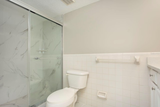 bathroom featuring tile walls, vanity, walk in shower, toilet, and a textured ceiling