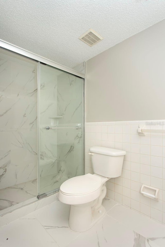 bathroom featuring a shower with shower door, tile walls, a textured ceiling, and toilet