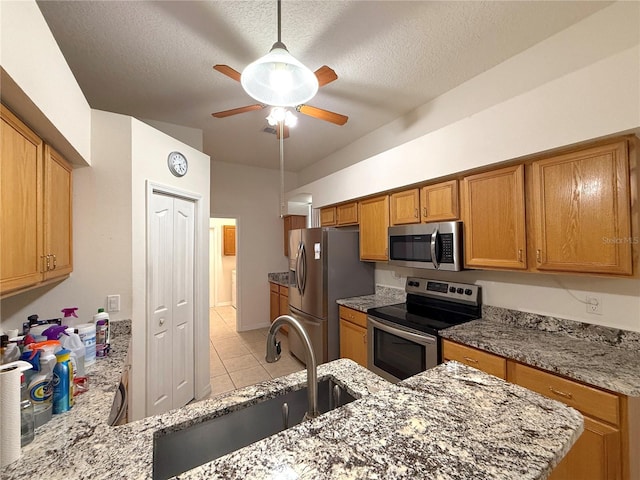 kitchen with appliances with stainless steel finishes, light stone countertops, sink, and a textured ceiling