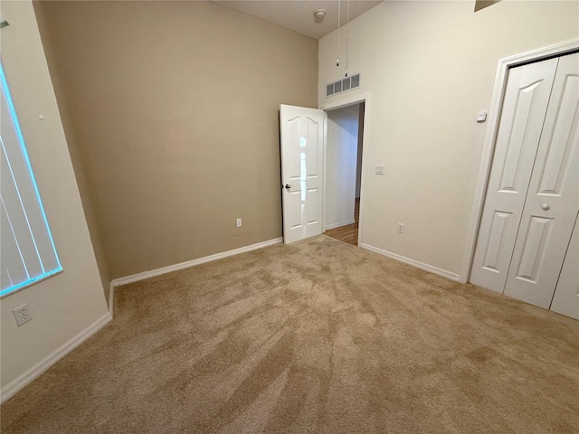 unfurnished bedroom with a high ceiling, light carpet, and a closet