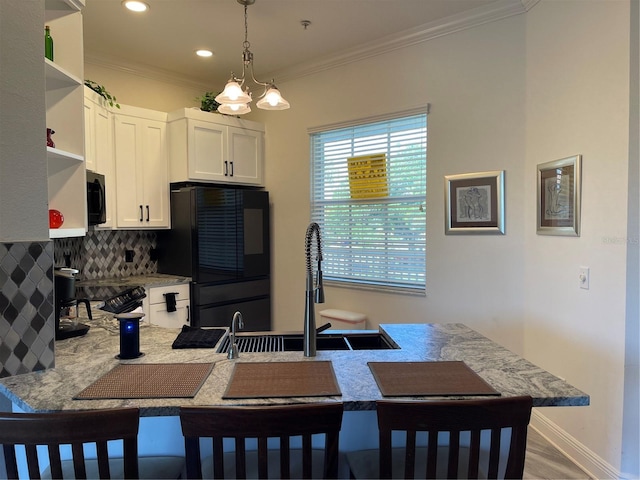 kitchen featuring a breakfast bar area, white cabinetry, ornamental molding, black fridge, and decorative light fixtures