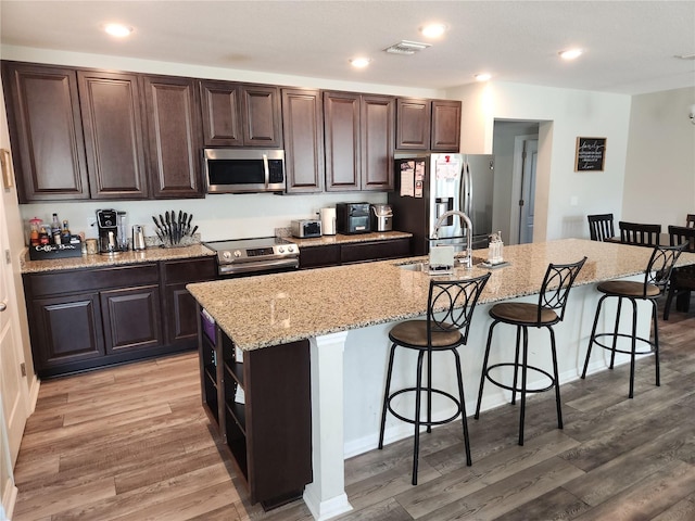 kitchen with a kitchen island with sink, dark brown cabinetry, a kitchen breakfast bar, and appliances with stainless steel finishes