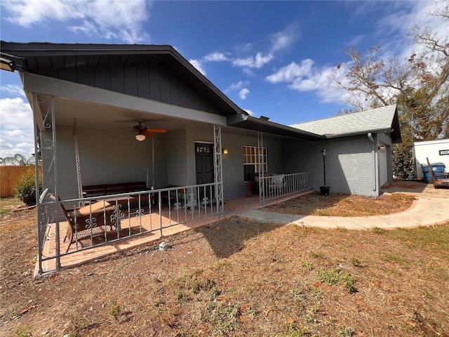 view of front facade with covered porch, ceiling fan, fence, and brick siding