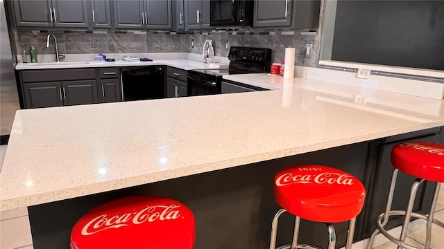 kitchen with a kitchen breakfast bar, light countertops, a sink, and black appliances