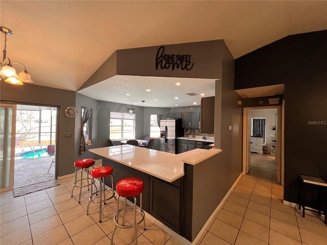 kitchen with vaulted ceiling, light countertops, light tile patterned floors, and a kitchen breakfast bar