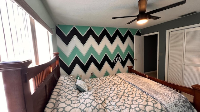 bedroom featuring wallpapered walls, an accent wall, visible vents, and a closet