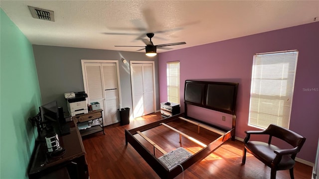 bedroom with a textured ceiling, visible vents, baseboards, multiple closets, and dark wood-style floors