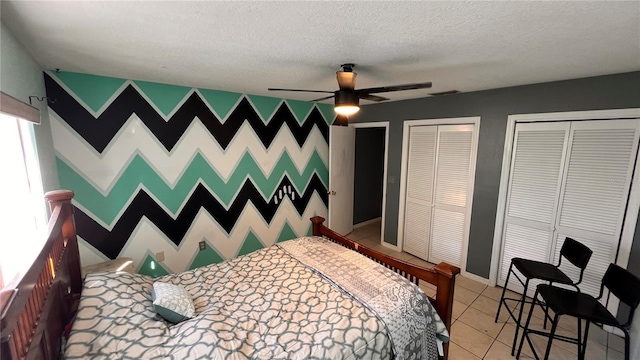 bedroom featuring light tile patterned floors, two closets, an accent wall, a textured ceiling, and wallpapered walls