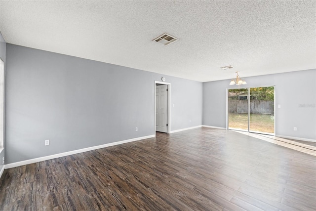 spare room featuring a textured ceiling, a notable chandelier, wood finished floors, visible vents, and baseboards