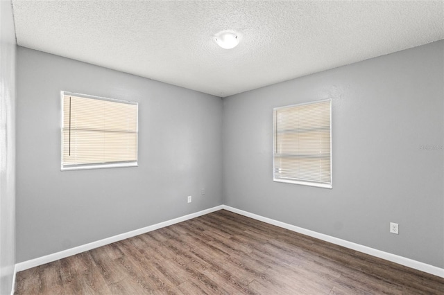 unfurnished room featuring plenty of natural light, a textured ceiling, baseboards, and wood finished floors