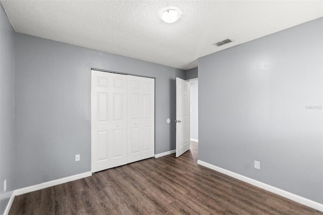 unfurnished bedroom with a closet, visible vents, a textured ceiling, wood finished floors, and baseboards