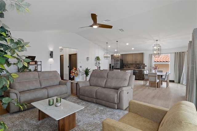 living room featuring lofted ceiling, ceiling fan with notable chandelier, and light hardwood / wood-style flooring