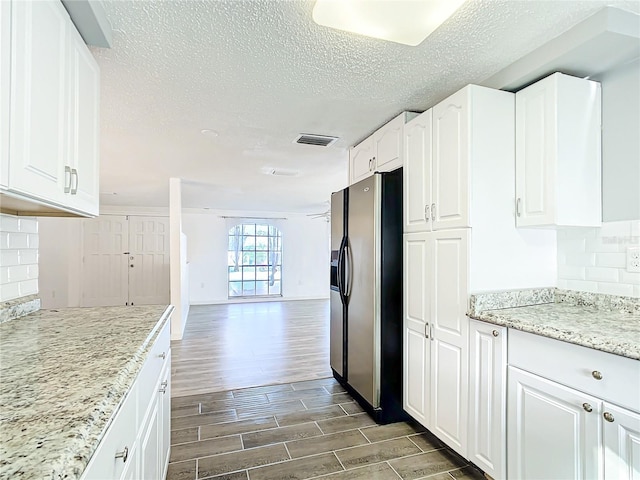 kitchen with stainless steel refrigerator with ice dispenser, white cabinetry, tasteful backsplash, and light stone counters