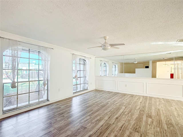 empty room with ceiling fan, wood-type flooring, a textured ceiling, and ornamental molding