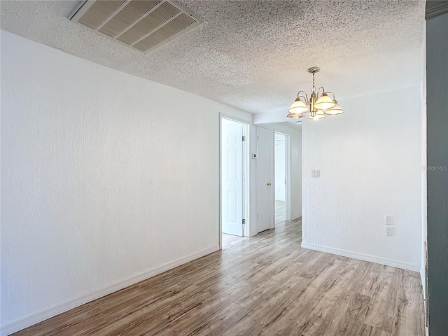 spare room featuring a textured ceiling, a chandelier, and light wood-type flooring