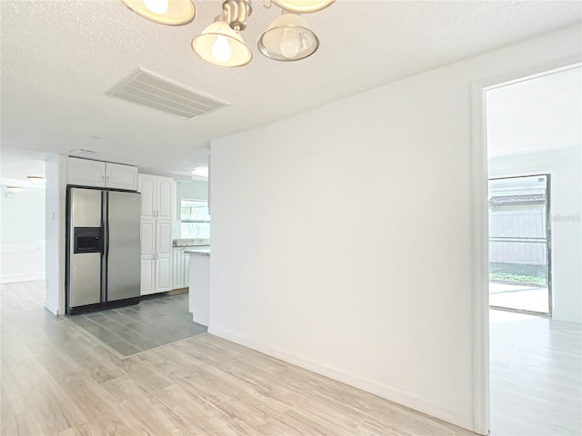 unfurnished room with an inviting chandelier, light hardwood / wood-style flooring, and a textured ceiling