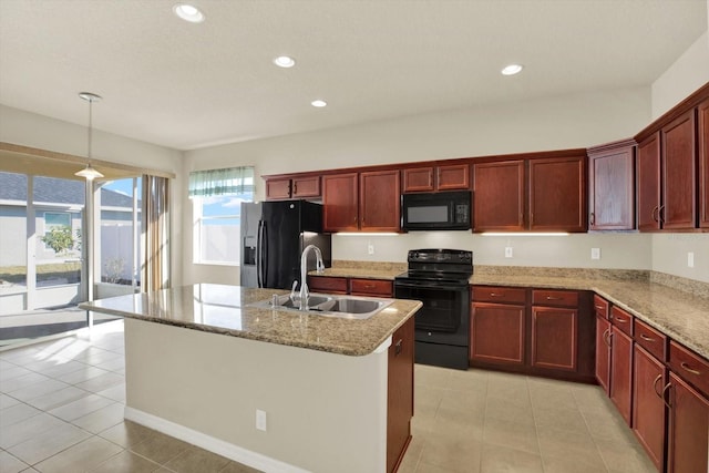 kitchen with decorative light fixtures, an island with sink, sink, black appliances, and light stone countertops