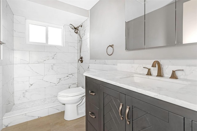 bathroom with vanity, toilet, tile walls, and a tile shower