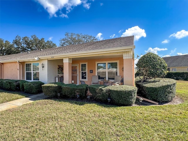 view of front of house featuring a shingled roof, a front lawn, and brick siding