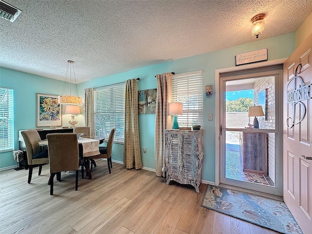 dining area featuring a textured ceiling, light wood-type flooring, visible vents, and baseboards