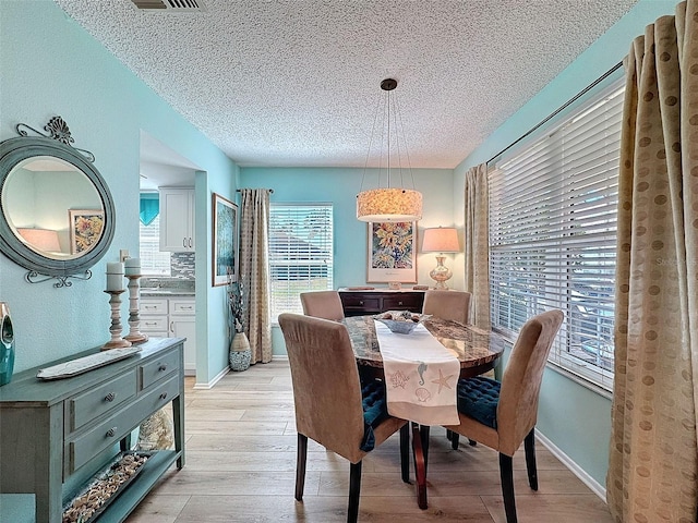 dining room with light wood-type flooring, a textured ceiling, and baseboards