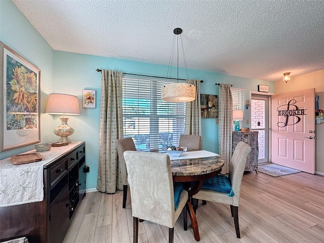 dining space with light wood-type flooring, baseboards, and a textured ceiling